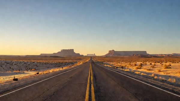 Empty two-lane desert highway stretching toward distant mesas under an open sky